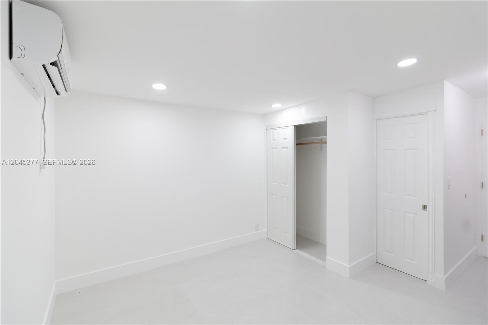 A minimalist white room features recessed lighting, a wall-mounted air conditioner, and two closet doors — 5803 Buchanan St, Hollywood FL 33021, HOLLYWOOD, FL