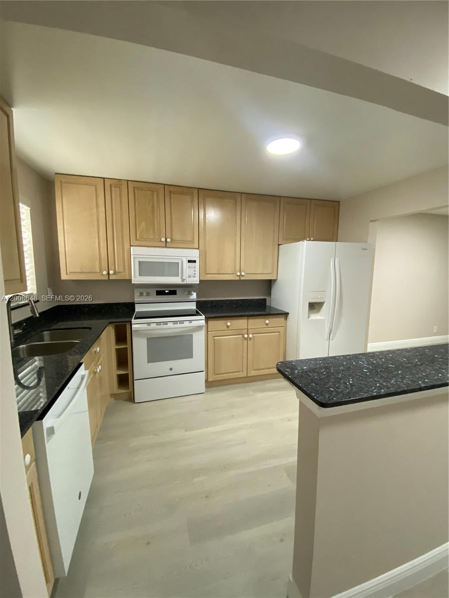 A kitchen features light wood cabinets, black countertops, white appliances, and light-colored wood-look flooring — 605 S State Road 7 # 3F, Margate FL 33068, MARGATE, FL