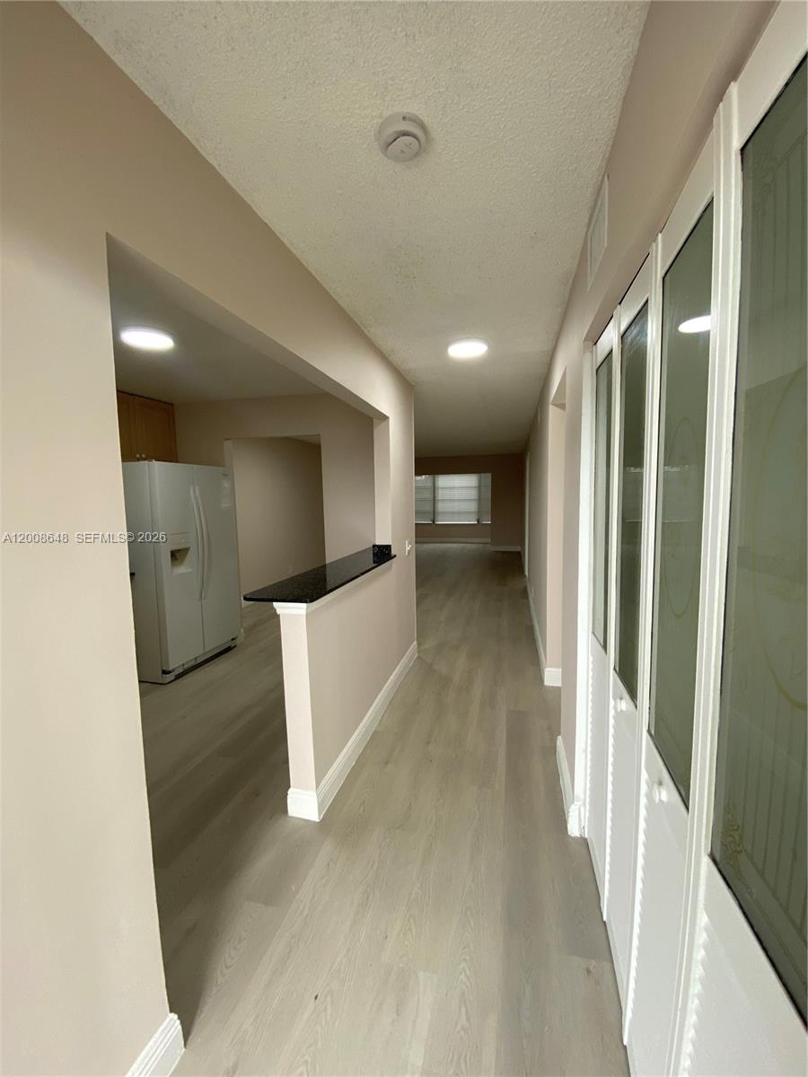 A hallway with light wood-look flooring leads toward a kitchen and a living area — 605 S State Road 7 # 3F, Margate FL 33068, MARGATE, FL