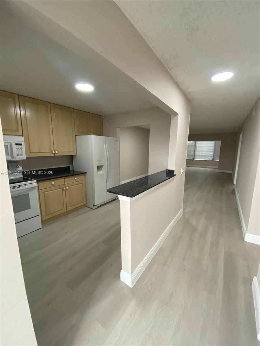 A kitchen with light wood cabinets and a black countertop opens into a living area — 605 S State Road 7 # 3F, Margate FL 33068, MARGATE, FL