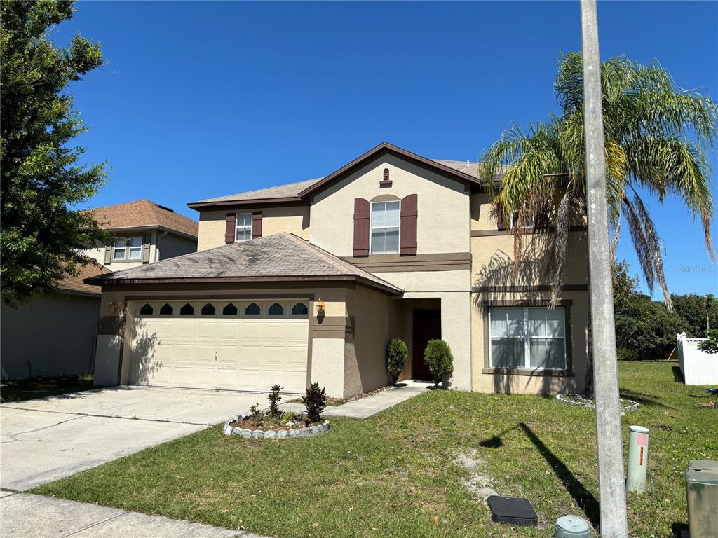 A two-story suburban house with a tan stucco exterior, a two-car garage, and a palm tree — 2872 PAYNES PRAIRIE CIRCLE, KISSIMMEE, FL
