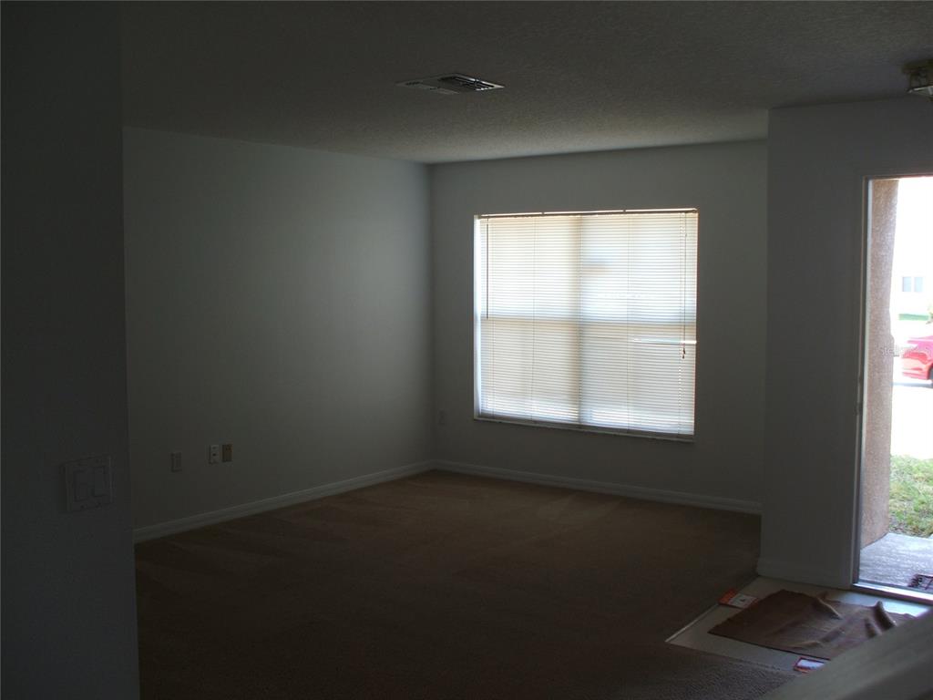 An empty room with beige carpet, white walls, a large window with blinds, and a door — 2872 PAYNES PRAIRIE CIRCLE, KISSIMMEE, FL