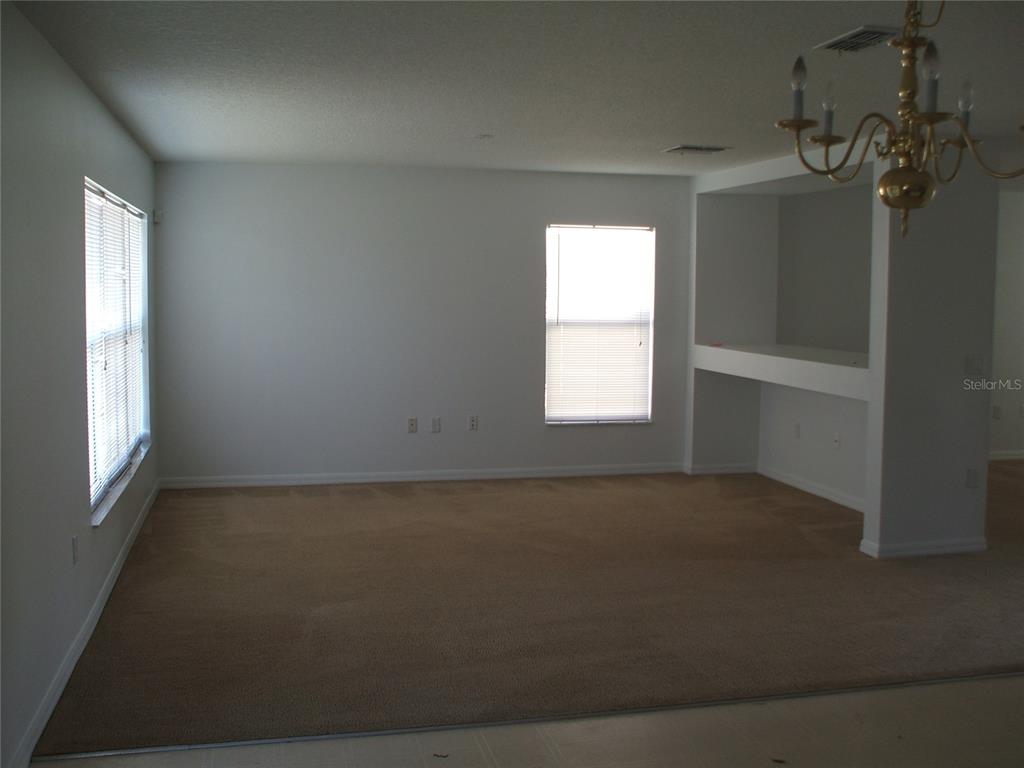 A carpeted living room features white walls, two windows with blinds, and a built-in alcove — 2872 PAYNES PRAIRIE CIRCLE, KISSIMMEE, FL