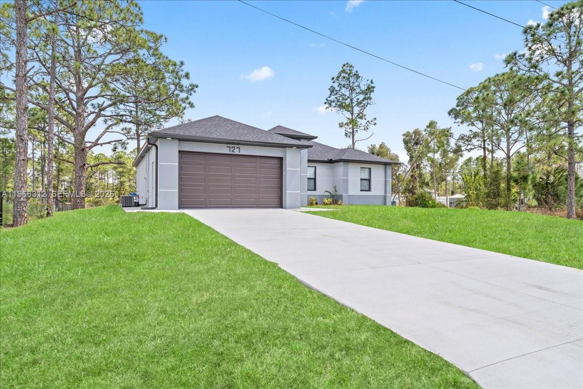 A single-story house with a brown garage door and gray exterior sits on a lawn — 727 Drury Ave, Lehigh Acres FL 33974, LEHIGH ACRES, FL