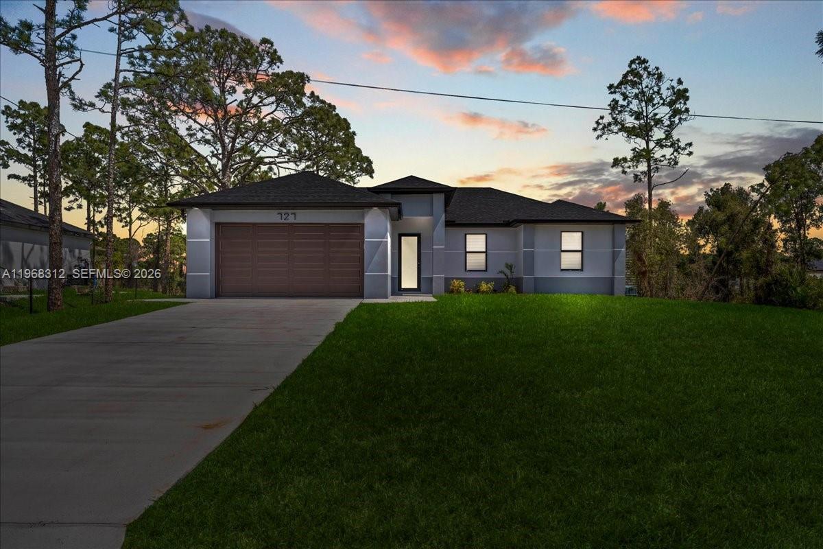A single-story house with a two-car garage and a concrete driveway at sunset — 727 Drury Ave, Lehigh Acres FL 33974, LEHIGH ACRES, FL