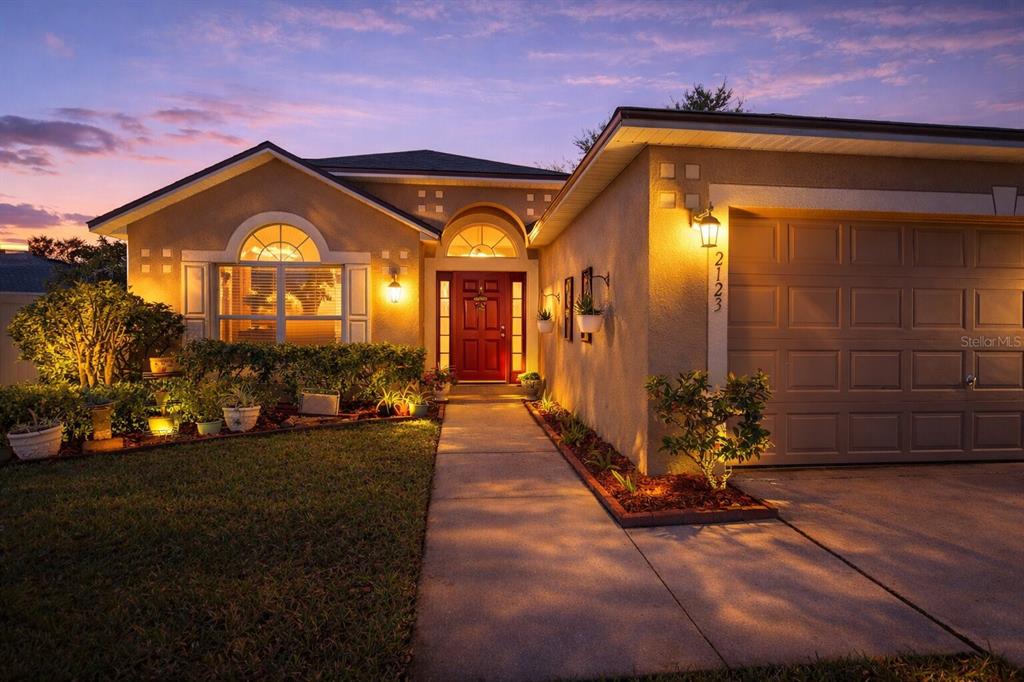 A single-story house with a red front door, arched windows, and an attached garage at dusk — 2123 ANOKA WAY, LEESBURG, FL