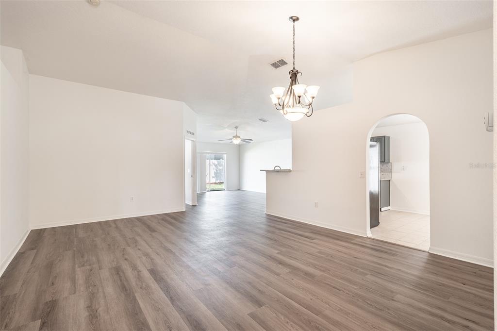 An open-concept living and dining area features light wood-look flooring and a central chandelier — 2123 ANOKA WAY, LEESBURG, FL
