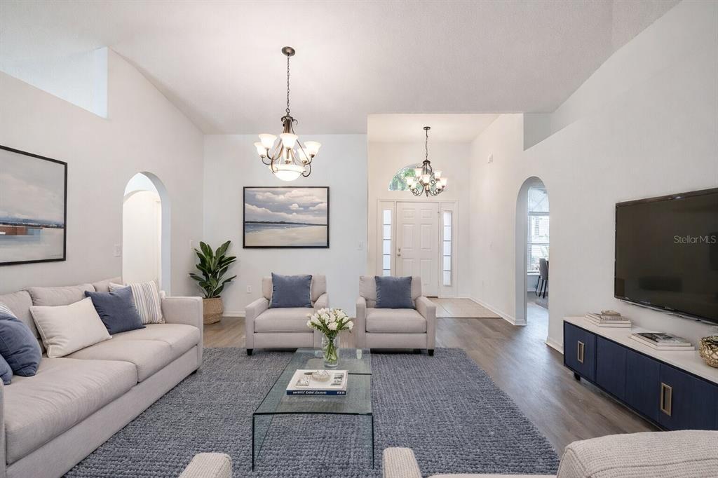 A bright living room features a grey sofa, two armchairs, a glass coffee table, and television — 2123 ANOKA WAY, LEESBURG, FL