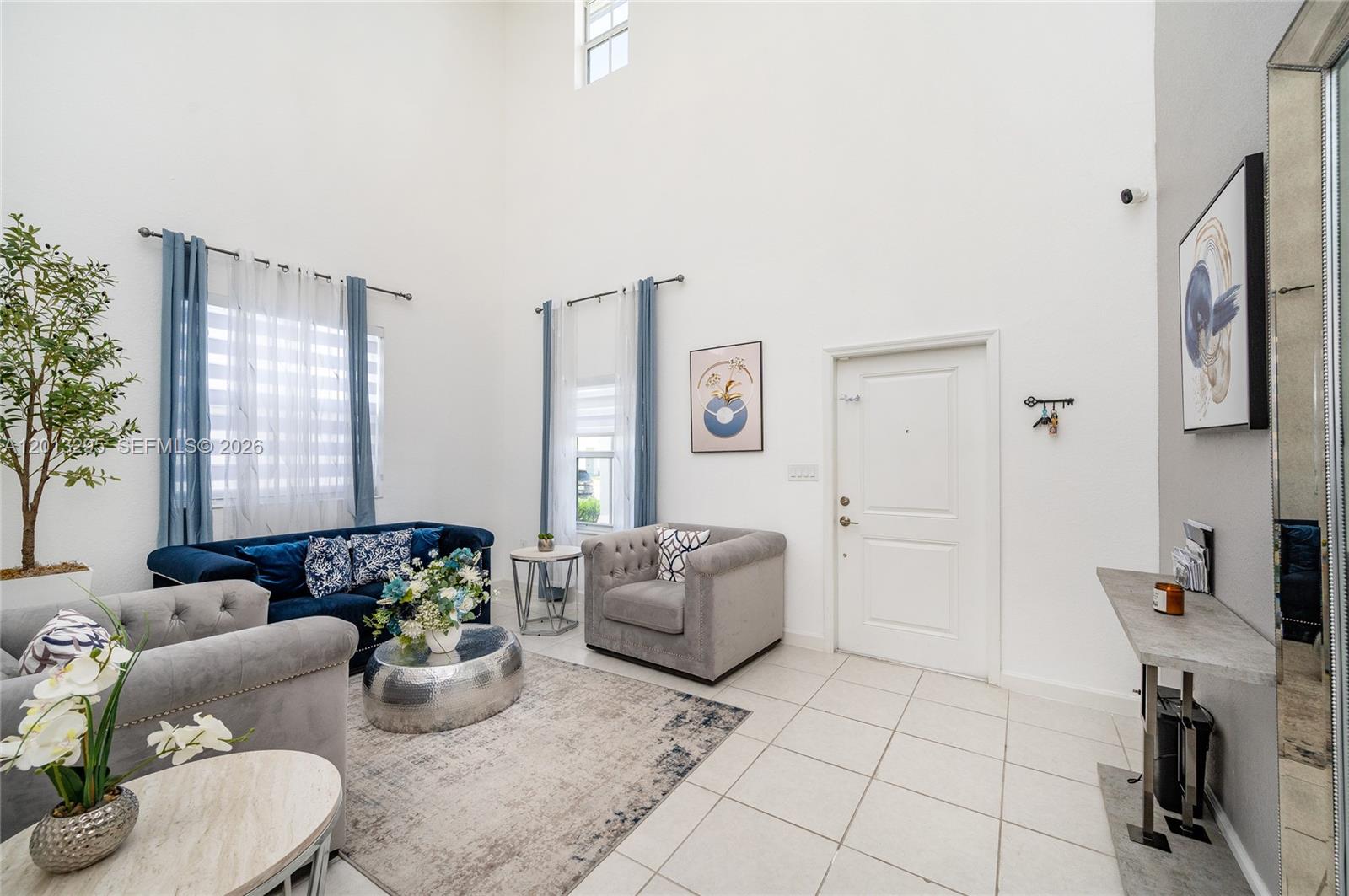 A living room with high ceilings, tile flooring, blue and grey furniture, and a front door — 21325 SW 127th Ct, Miami FL 33177, MIAMI, FL