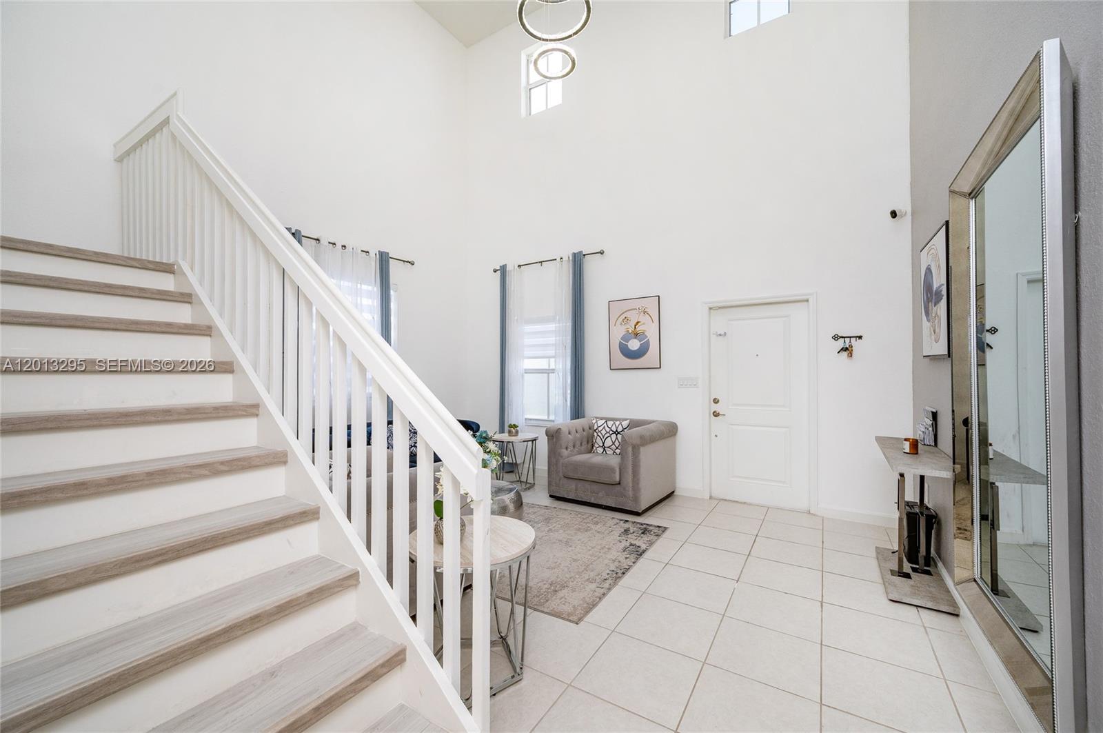 A bright entryway features a staircase, tiled floors, and a tall ceiling with a chandelier — 21325 SW 127th Ct, Miami FL 33177, MIAMI, FL