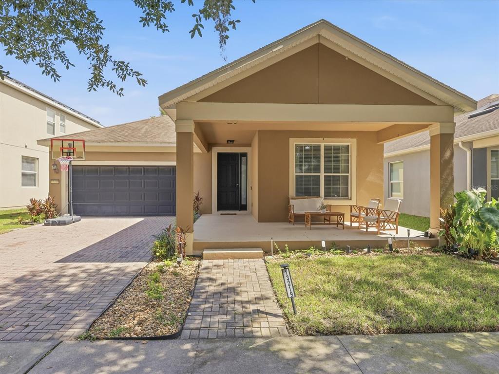 A single-story house with a tan exterior, a covered front porch, and a brick driveway — 13219 CHARFIELD STREET, WINDERMERE, FL