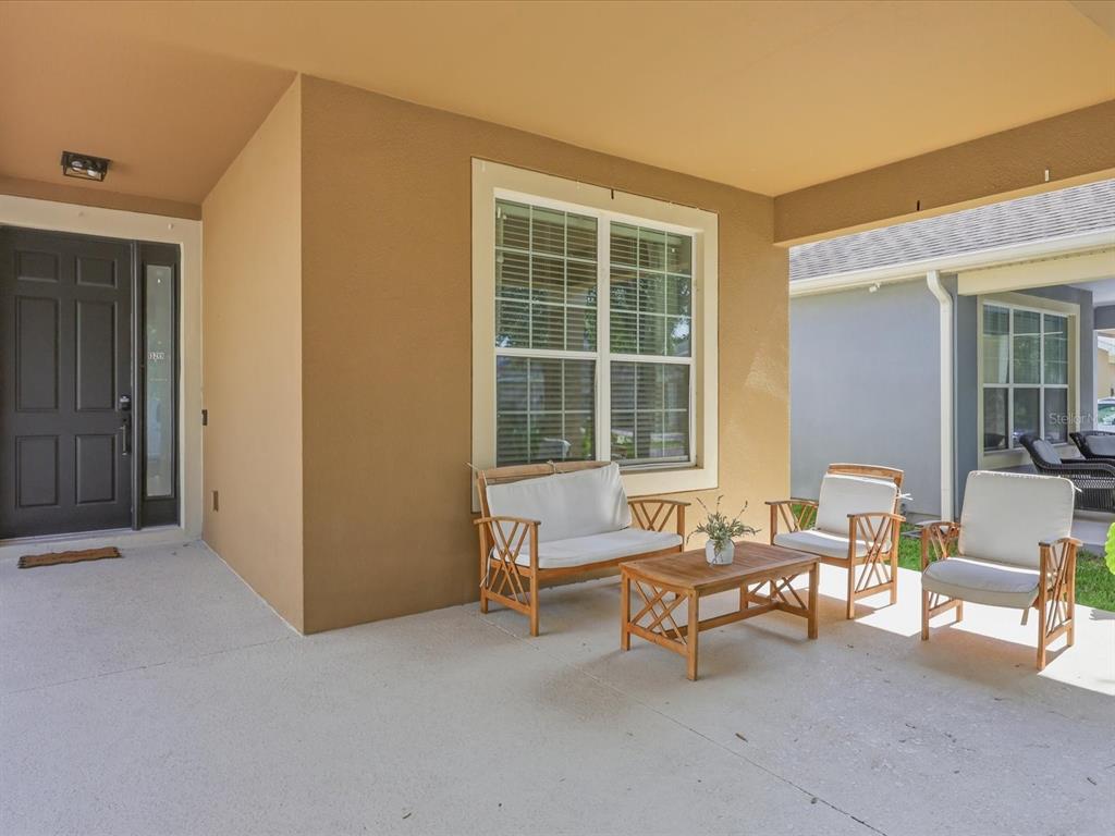 A covered front porch features a dark door, a window, and outdoor wooden furniture — 13219 CHARFIELD STREET, WINDERMERE, FL