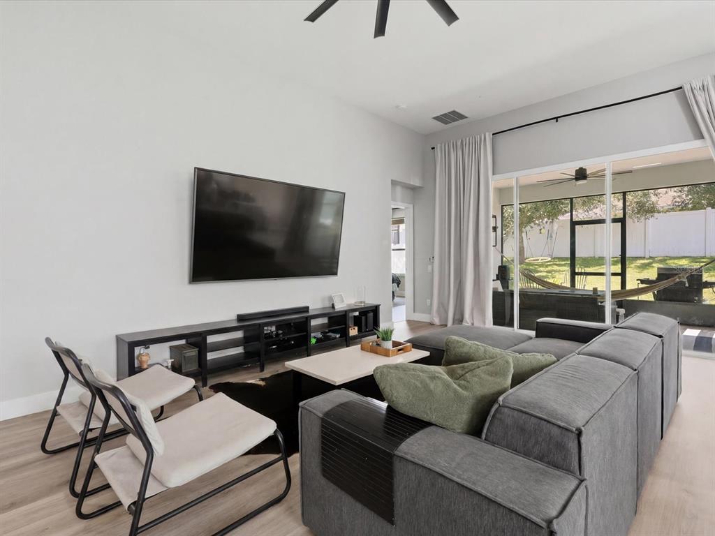 A living room features a wall-mounted television, a grey sectional sofa, and sliding glass doors — 13219 CHARFIELD STREET, WINDERMERE, FL