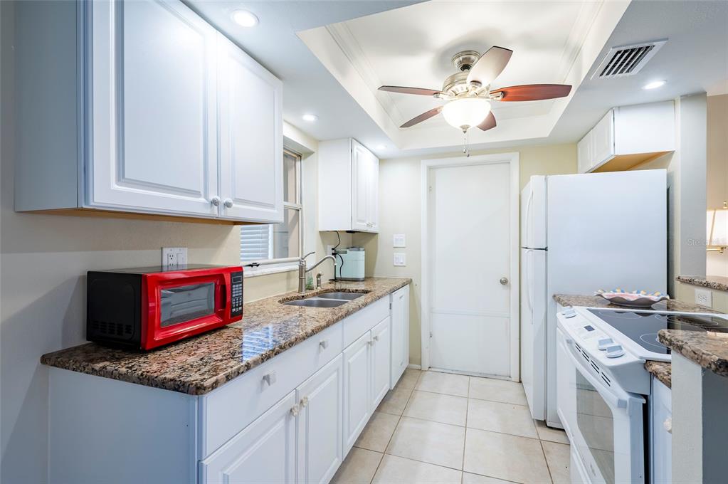 A kitchen features white cabinets, granite countertops, a red microwave, and a ceiling fan — 4479 MICHIGAN LANE, CLEARWATER, FL