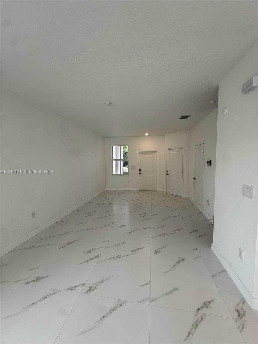 A long, empty room features white walls and large, white marble-patterned floor tiles — 2427 NW 131st Cir, Miami FL 33167, MIAMI, FL