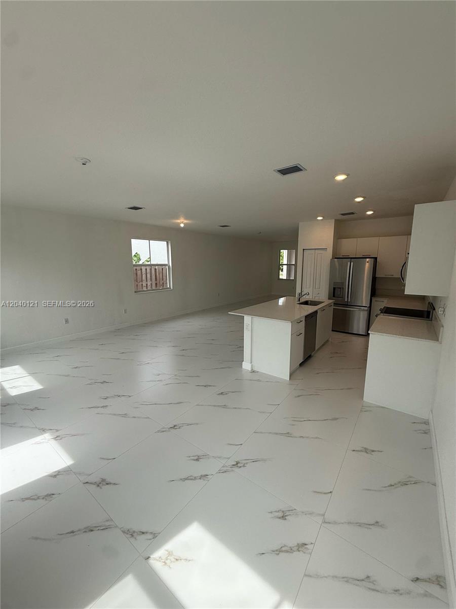 An open-concept kitchen and living area features white marble-look tile flooring and white cabinetry — 2427 NW 131st Cir, Miami FL 33167, MIAMI, FL