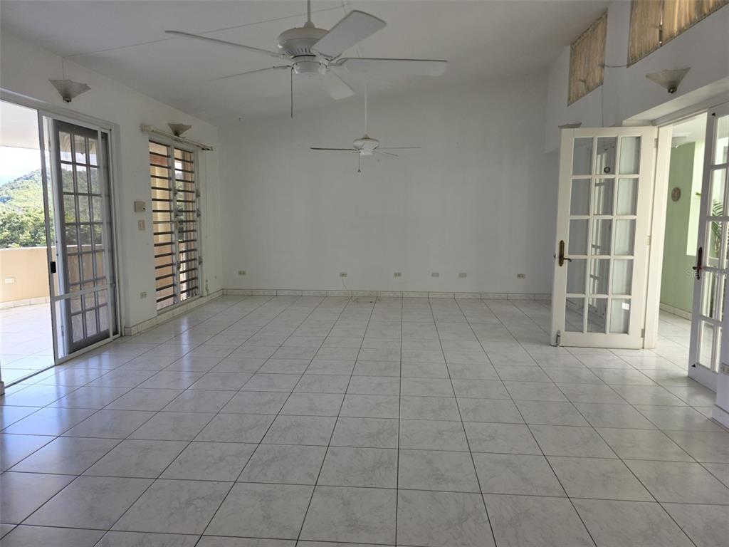 An empty room features white tile flooring, two ceiling fans, and glass-paned doors leading outside — 17 DEL RECREO, CAGUAS, PR