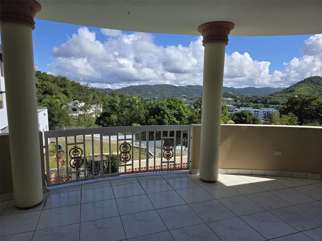 A tiled balcony features two large columns and a metal railing overlooking a mountainous landscape — 17 DEL RECREO, CAGUAS, PR