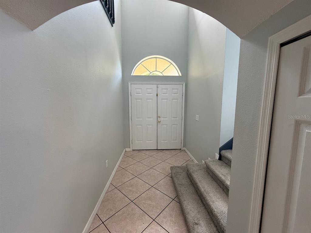 An entryway features a double door, a high ceiling, tile flooring, and carpeted stairs — 162 HARWOOD CIRCLE, KISSIMMEE, FL