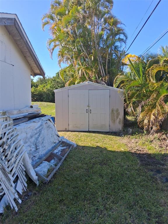 A beige storage shed sits in a grassy backyard next to a white building — 3311 ASH STREET, PUNTA GORDA, FL