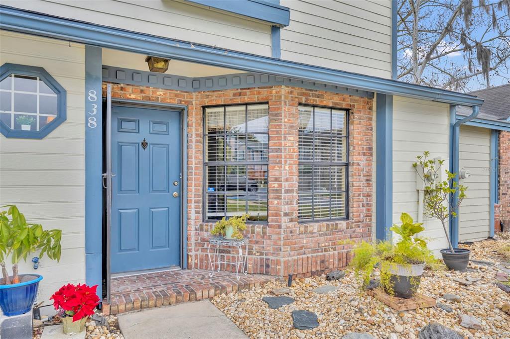 A blue front door and brick bay window are set against light-colored siding — 838 COMMONWEALTH COURT, CASSELBERRY, FL