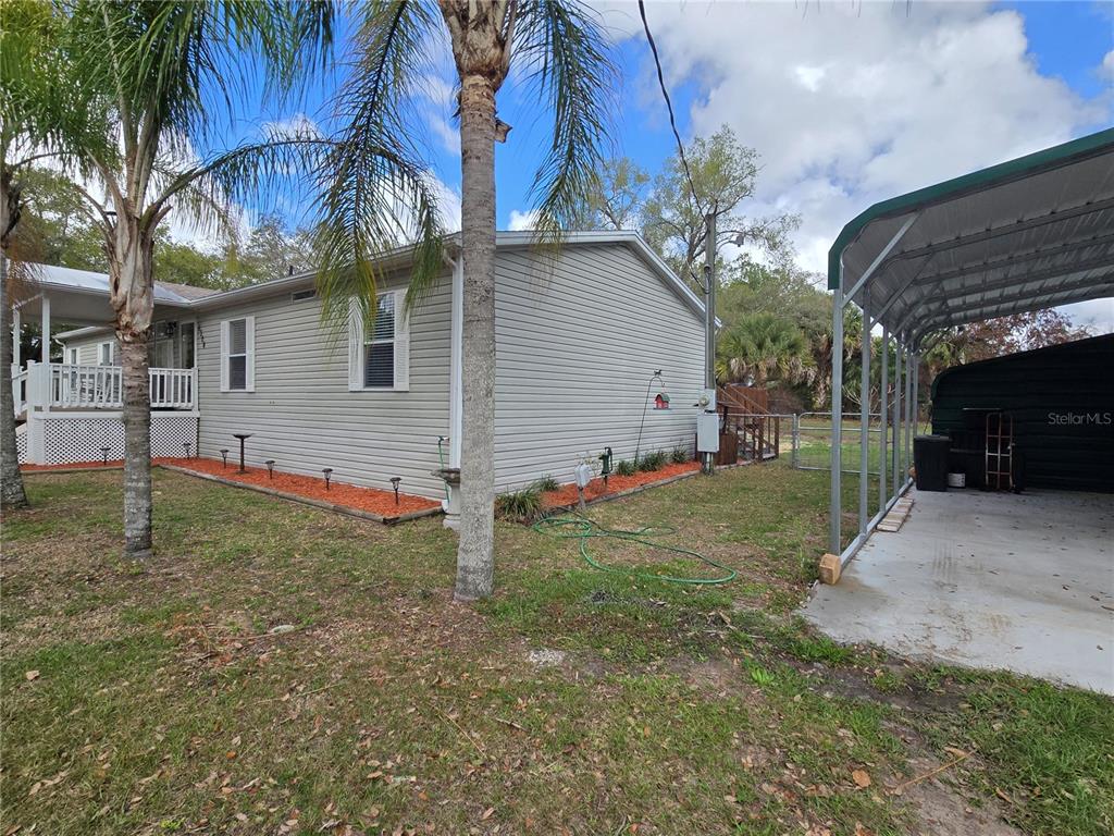 A light gray siding house features a side porch, a carport, and orange mulch landscaping — 5304 FAIRMONT ROAD, LAKE WALES, FL