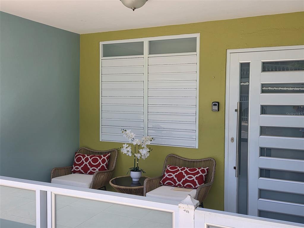 A covered patio features two wicker chairs, a small table, and a white front door — Calle Bilbao SECTOR PLAYUELA, AGUADILLA, PR