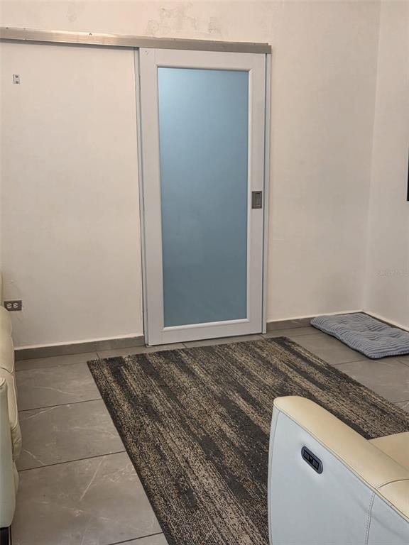A room with light gray tile flooring, a textured area rug, and a white sliding door — Calle Bilbao SECTOR PLAYUELA, AGUADILLA, PR