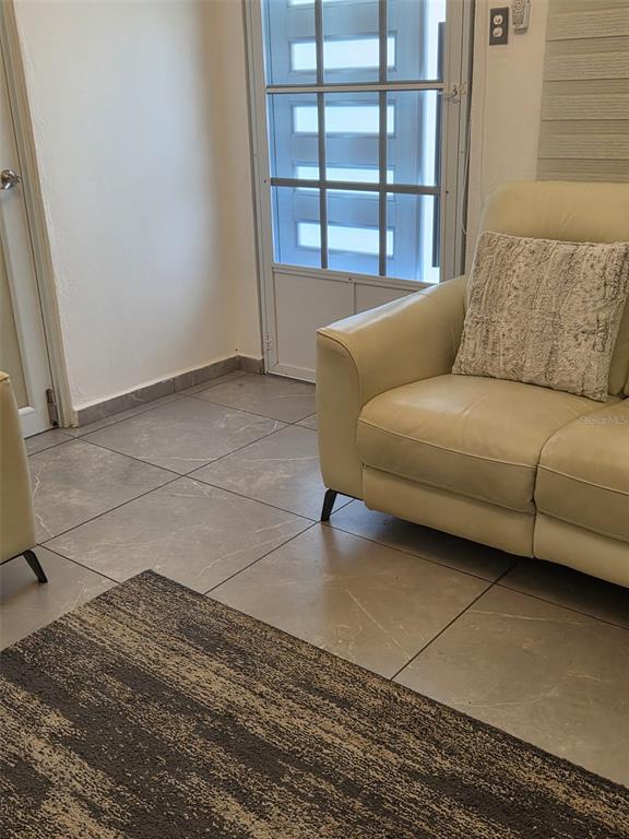 A light-colored leather sofa sits on a tiled floor next to a glass-paneled door — Calle Bilbao SECTOR PLAYUELA, AGUADILLA, PR