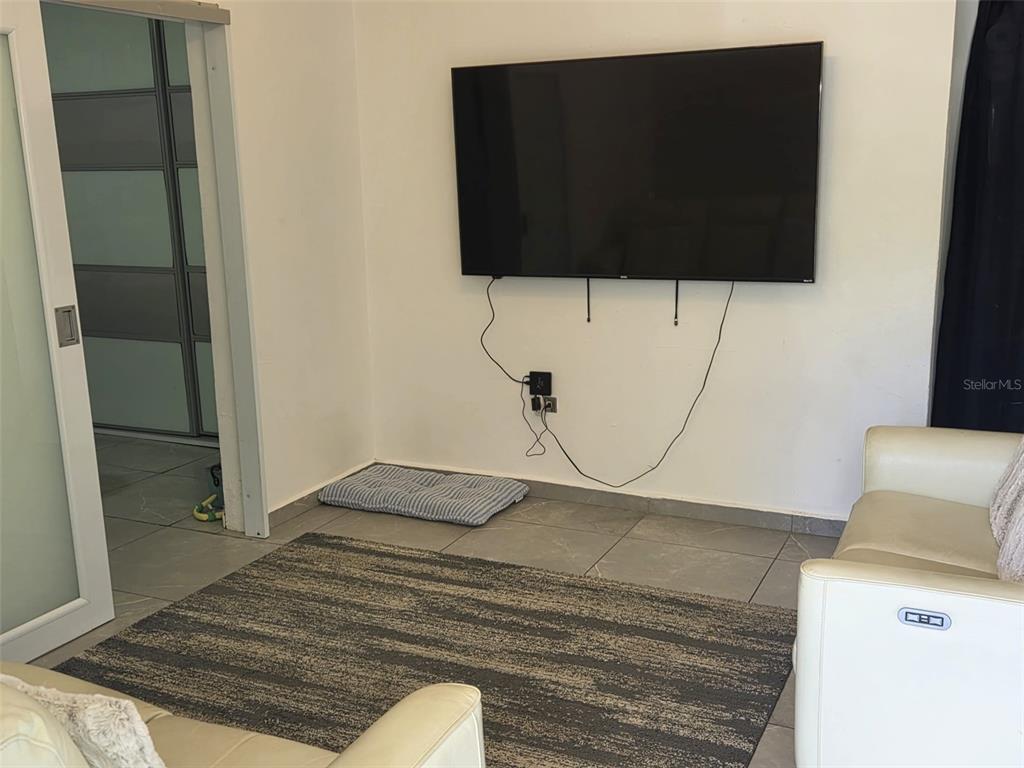 A living room features a wall-mounted television, tile flooring, and a large area rug — Calle Bilbao SECTOR PLAYUELA, AGUADILLA, PR