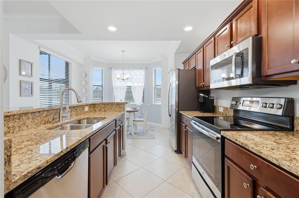 A kitchen with granite countertops, wood cabinets, stainless steel appliances, and an adjacent dining area — 16804 VARDON TERRACE UNIT 103, BRADENTON, FL