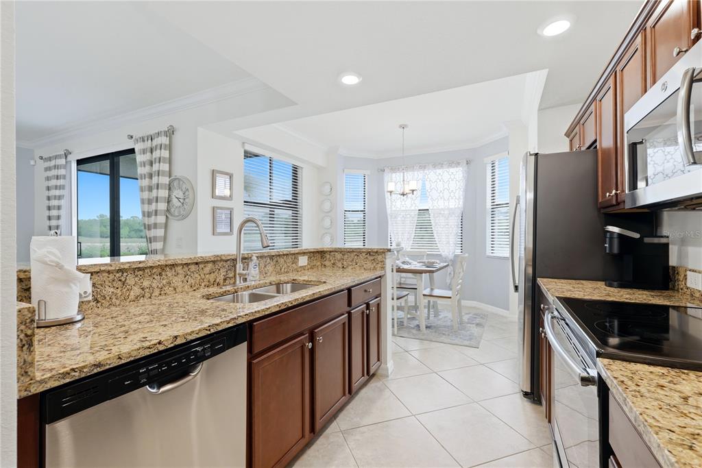 A kitchen with granite countertops, dark wood cabinets, and stainless steel appliances overlooks a dining area — 16804 VARDON TERRACE UNIT 103, BRADENTON, FL