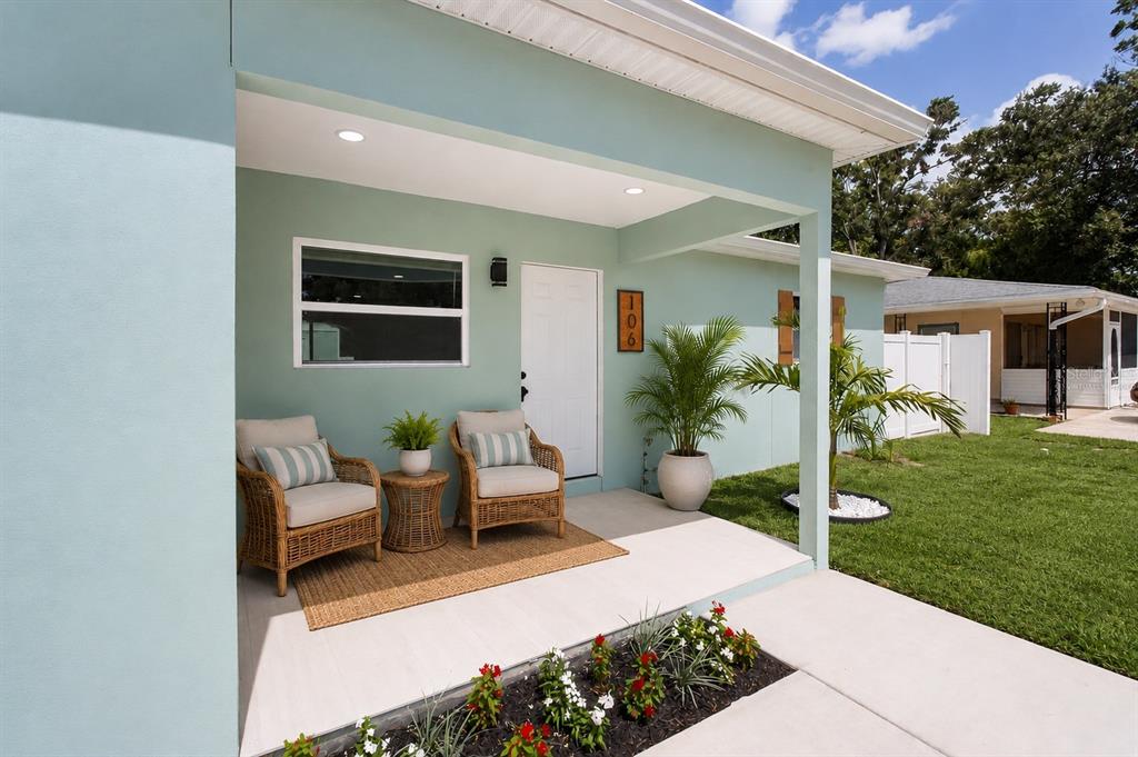 A covered front porch features two wicker chairs, a small table, and a potted palm — 106 MELODY LANE, LARGO, FL