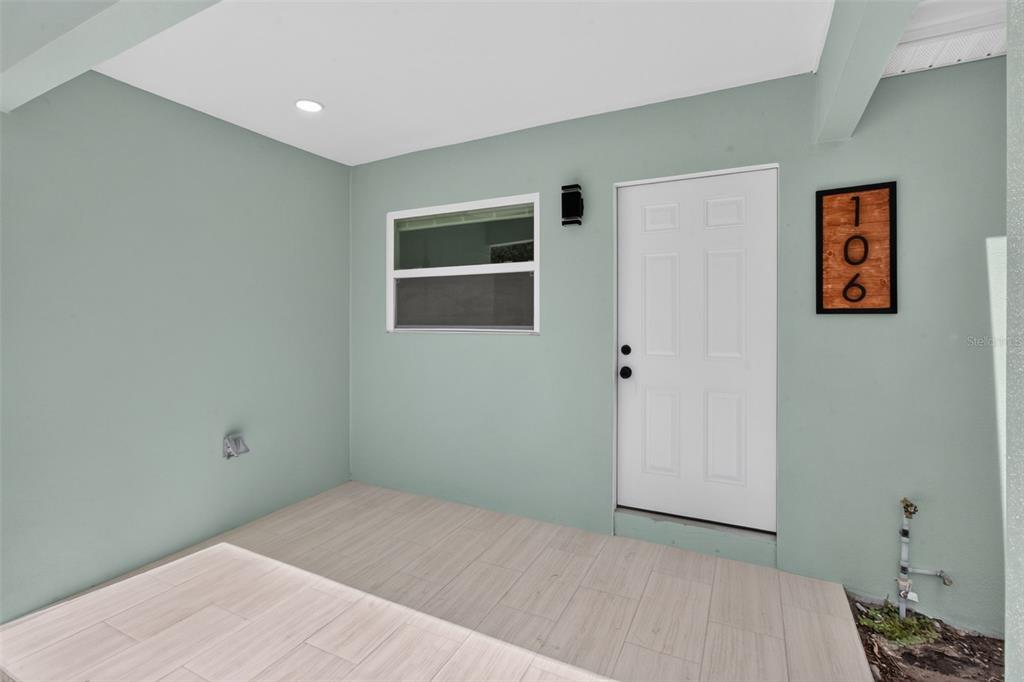 A covered entryway features light green walls, a white door, and light-colored wood-look tile flooring — 106 MELODY LANE, LARGO, FL