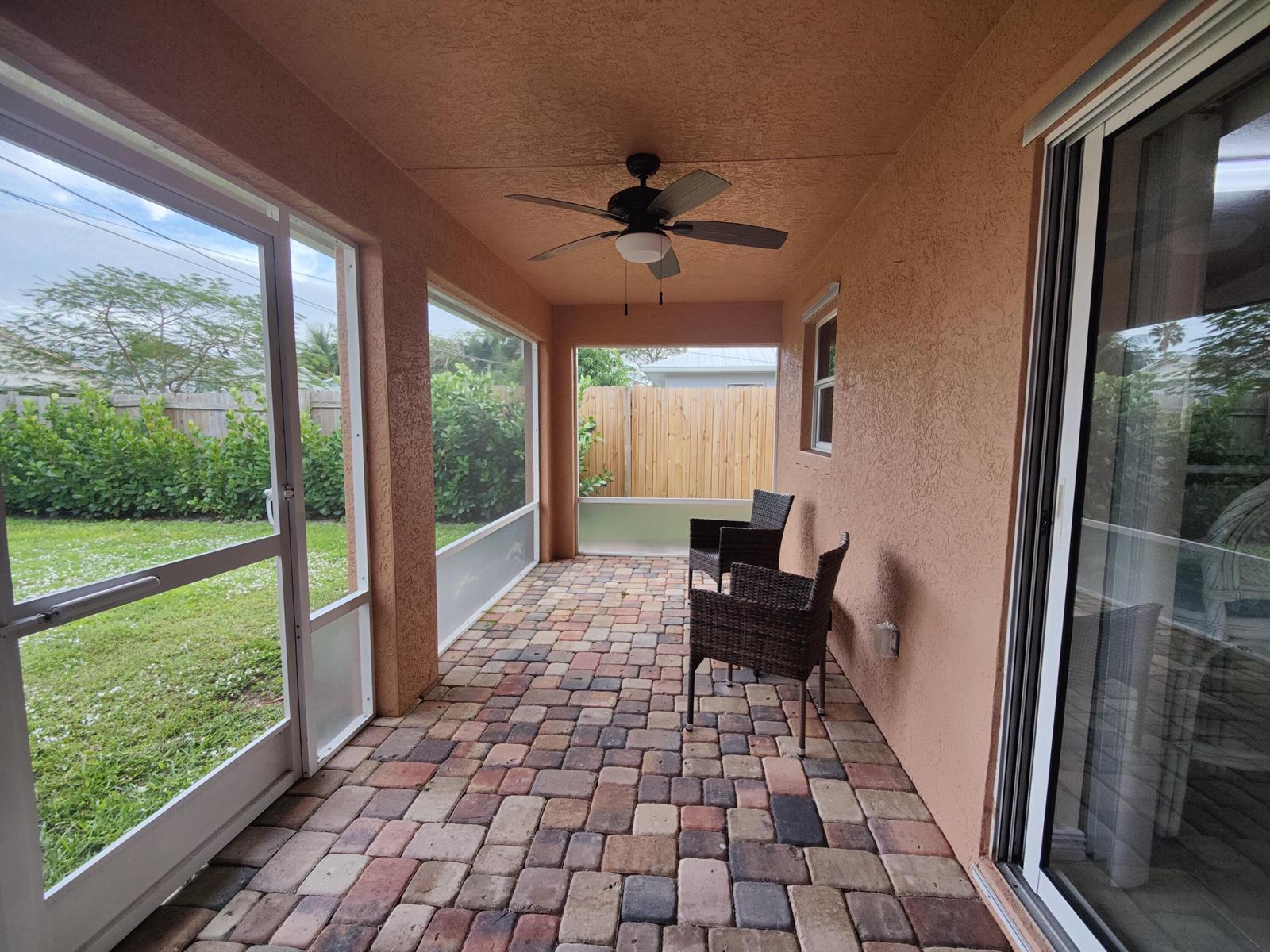 A covered patio with brick pavers, a ceiling fan, and screen walls overlooking a yard — 5795 SE Mitzi Lane, Stuart FL 34997, STUART, FL