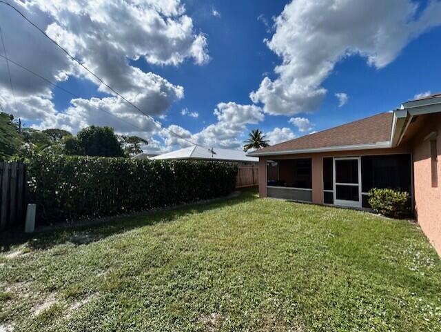 A backyard with a grassy lawn, a screened-in patio, and a tall hedge fence — 5795 SE Mitzi Lane, Stuart FL 34997, STUART, FL