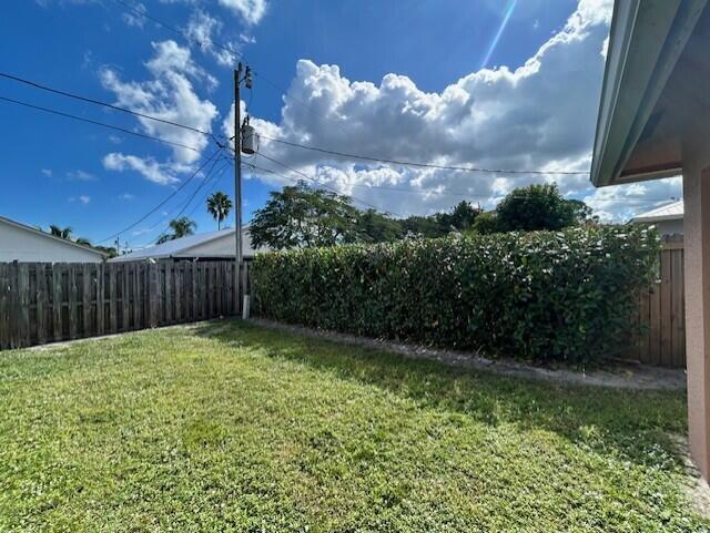 A grassy backyard features a wooden fence, a tall hedge, and a utility pole — 5795 SE Mitzi Lane, Stuart FL 34997, STUART, FL