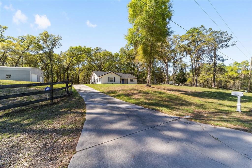 A concrete driveway leads to a single-story house with a detached garage and fenced yard — 13740 SW 49TH PLACE, OCALA, FL
