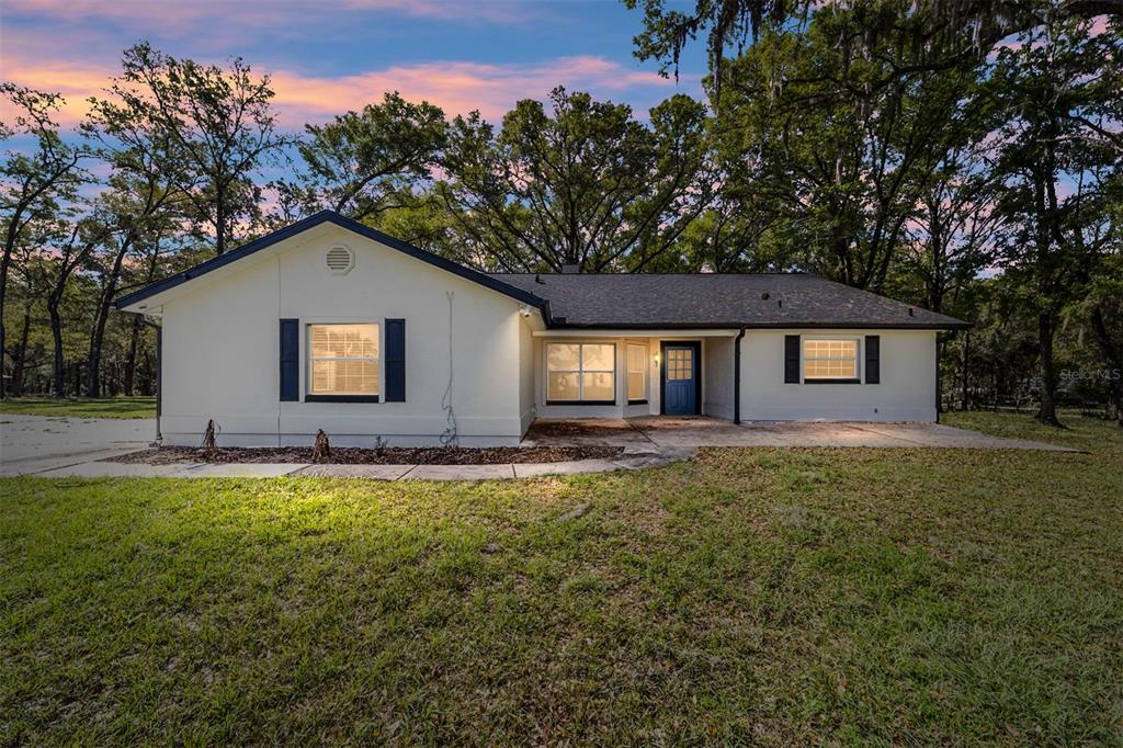 A single-story house with white stucco walls, a dark roof, and a blue front door — 13740 SW 49TH PLACE, OCALA, FL