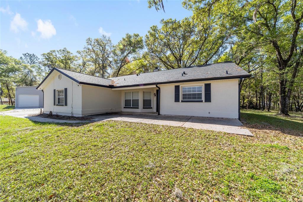 A single-story house with a light-colored exterior, dark roof, and a concrete patio — 13740 SW 49TH PLACE, OCALA, FL