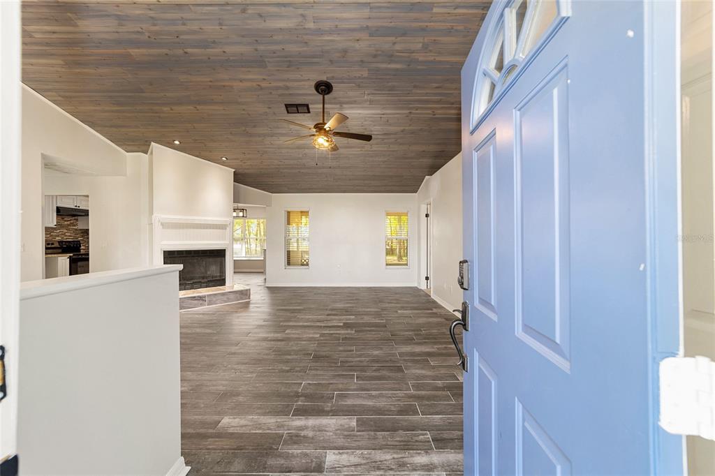 A view from an open blue front door into a living room with wood-look flooring — 13740 SW 49TH PLACE, OCALA, FL