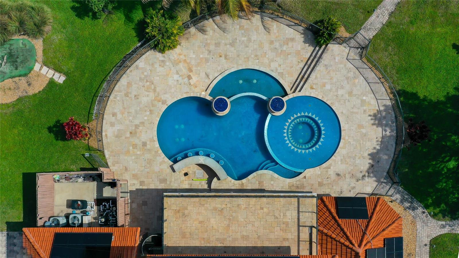 An aerial view shows a custom-shaped swimming pool with a spa and stone patio — 5660 Lago Del Sol Drive, Lake Worth FL 33449, LAKE WORTH, FL