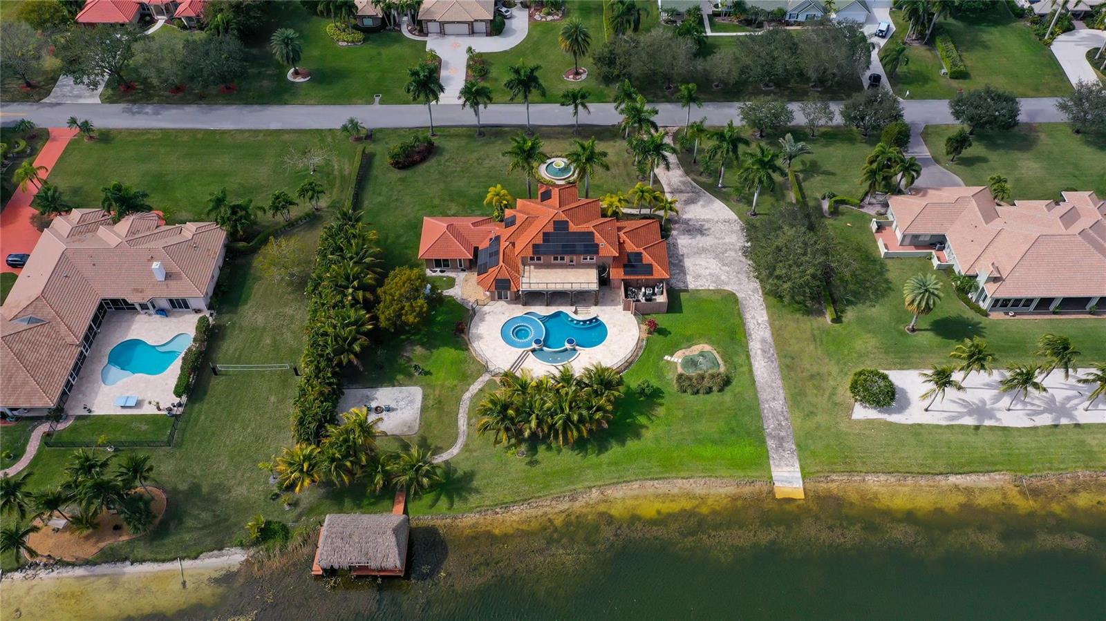 An aerial view shows a large house with a red roof, pool, and waterfront dock — 5660 Lago Del Sol Drive, Lake Worth FL 33449, LAKE WORTH, FL