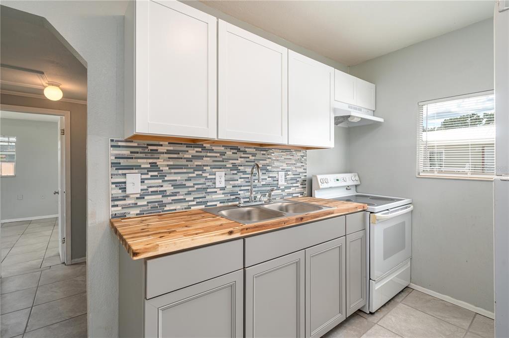 A kitchen features gray lower cabinets, white upper cabinets, a wood countertop, and tiled backsplash — 520 W JACKSON AVENUE, LAKE WALES, FL