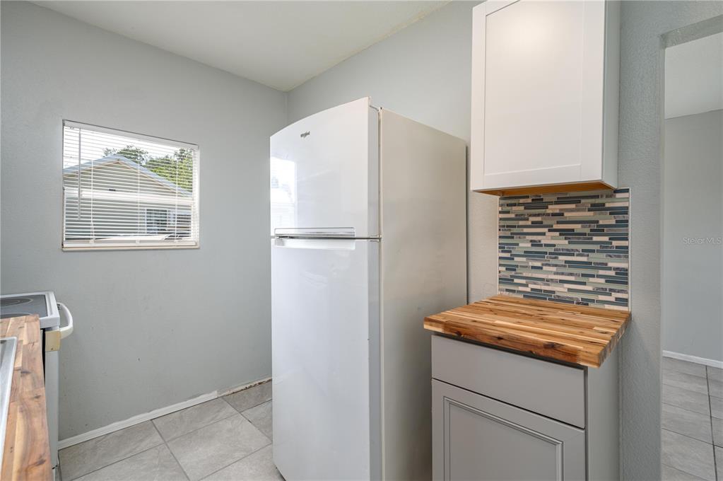A kitchen features a white refrigerator, gray cabinets, a wood countertop, and a tiled backsplash — 520 W JACKSON AVENUE, LAKE WALES, FL