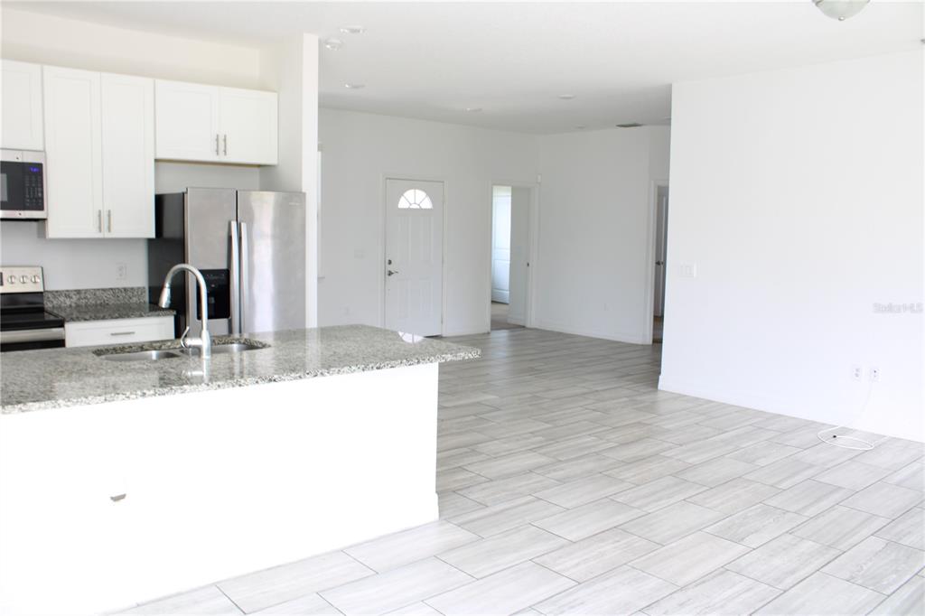 A kitchen with granite countertops and stainless steel appliances opens into a tiled living area — 104 HERRING WAY, KISSIMMEE, FL