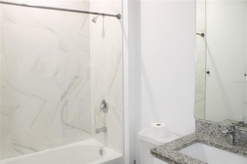 A bathroom features a white tiled shower-tub combo, a granite vanity, and a toilet — 104 HERRING WAY, KISSIMMEE, FL