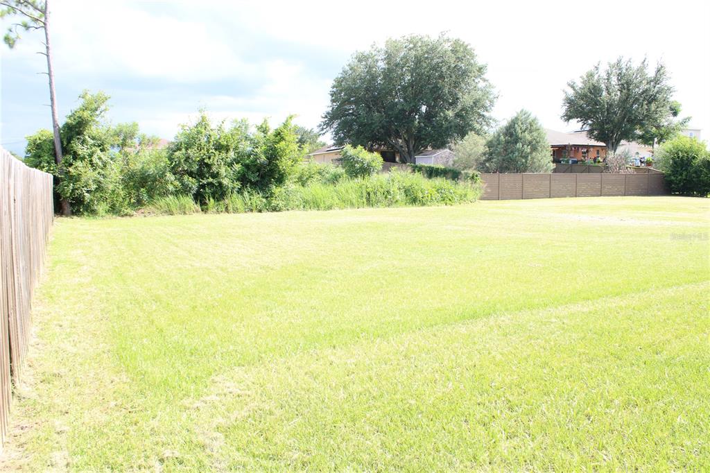 A large, flat, grassy backyard is enclosed by a wooden fence with trees in the background — 104 HERRING WAY, KISSIMMEE, FL