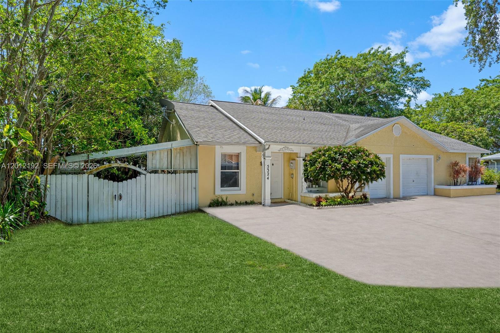 A yellow single-story house features a concrete driveway, a white fence, and two garage doors — 5324 GRAY FOX CT, West Palm Beach FL 33415, WEST PALM BEACH, FL