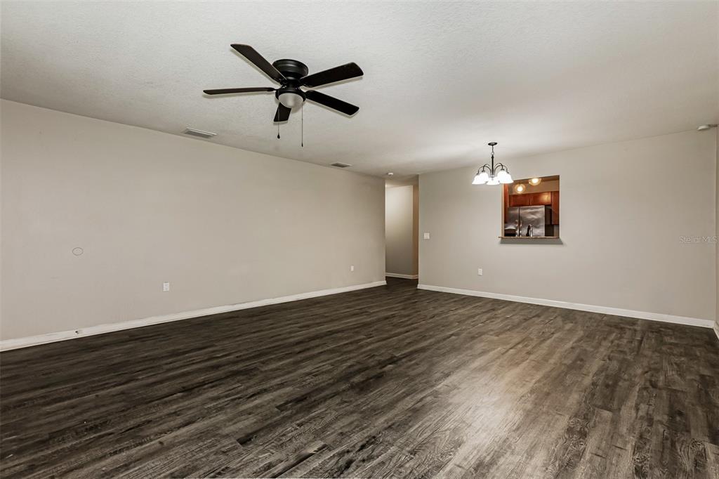 An empty living room features dark wood-look flooring, a ceiling fan, and a kitchen pass-through — 1505 E CARACAS STREET, TAMPA, FL